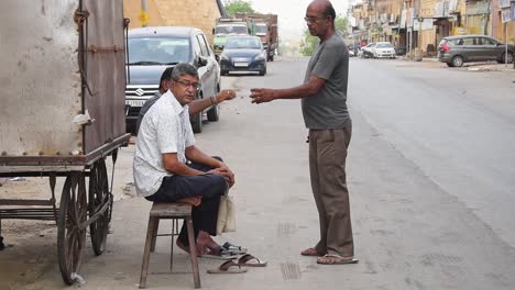 A-man-is-offering-tea-to-his-friends-in-a-disposable-cup-while-sitting-on-a-bench-on-the-side-of-a-road