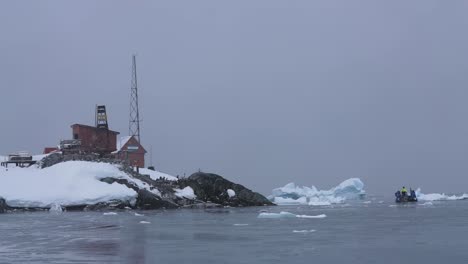 Base-Marrón-En-La-Costa-Antártica,-Edificio-De-Estaciones-Y-Personas-En-Bote,-Hielo-Y-Nieve-A-60-Fps