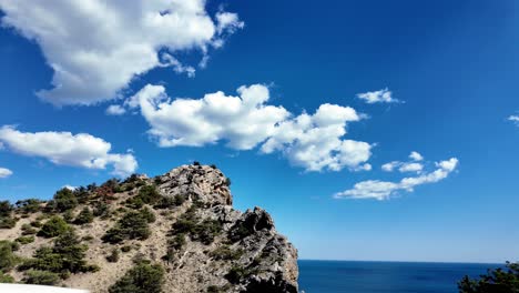 A-scenic-view-of-a-rocky-mountaintop-overlooking-the-ocean-with-a-clear-blue-sky-and-white-clouds