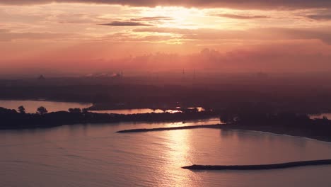 Wide-drone-shot-of-a-boat-leaving-the-harbor-during-a-beautiful-orange-sunset-reflecting-on-the-ocean