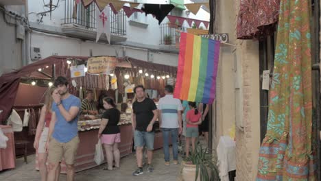 Gente-Paseando-Por-Un-Mercado-Medieval-Junto-A-Una-Bandera-Del-Orgullo-Gay