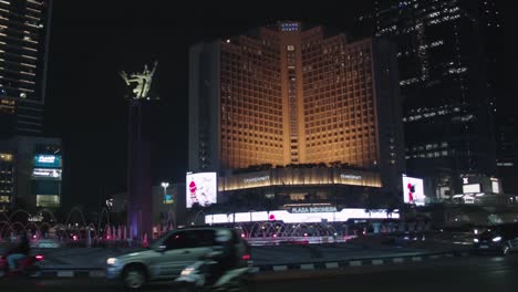 Vista-Nocturna-Del-Hotel-Indonesia-En-Yakarta-Con-Tráfico-Y-Emblemático-Monumento-De-Bienvenida-Iluminado