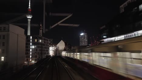 Train-driving-at-night-through-Berlin,-Germany,-view-on-Fernsehturm-television-tower,-another-train-is-passing,-u-bahn