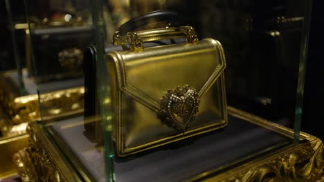 Golden-dolce-and-gabbana-bag-standing-in-a-glass-display-case,-surrounded-by-golden-decorations