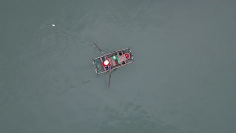 Toma-Aérea-De-Una-Mujer-Remando-Su-Bote-A-Través-De-Un-Pueblo-Pesquero-Flotante-En-Cat-Ba-Y-La-Bahía-De-Halong-En-El-Norte-De-Vietnam