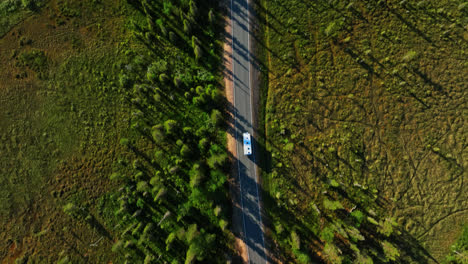 Top-down-drone-shot-above-a-RV-passing-arctic-wetlands-of-Lapland,-summer-evening