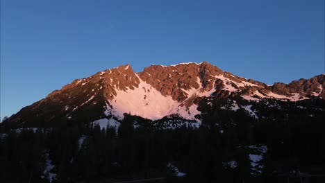 Toma-Aérea-De-Drones-De-La-Montaña-Roja-Desde-El-Amanecer,-Paisaje-Montañoso-Invernal-Rodeado-De-Bosque