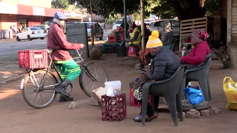 La-Gente-Al-Lado-De-Una-Calle-Muy-Transitada-Se-Sienta-Y-Habla-Entre-Sí,-El-Hombre-Llega-En-Bicicleta-Para-Saludarlos.