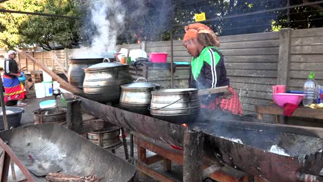 Una-Mujer-Africana-Cocinando-Comida-En-Ollas-De-Hierro-Fundido-En-Un-Mercado.