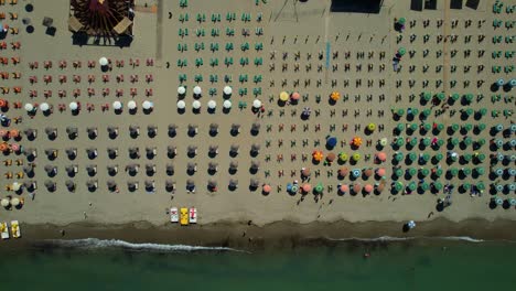 Aerial-view-of-beach-umbrellas-in-a-row-on-the-sandy-beach-kissed-by-the-Adriatic-Sea,-creating-a-picturesque-background