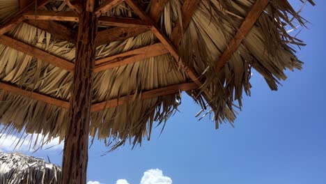 Straw-beach-umbrellas-in-slight-breeze,-vacation-under-blue-sky