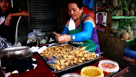 ANTIPOLO-CITY,-PHILIPPINES-–-JULY-12,-2019:-A-street-food-vendor-puts-deep-fried-chicken-intestine-into-barbecue-sticks-and-sells-them-at-her-makeshift-food-stall