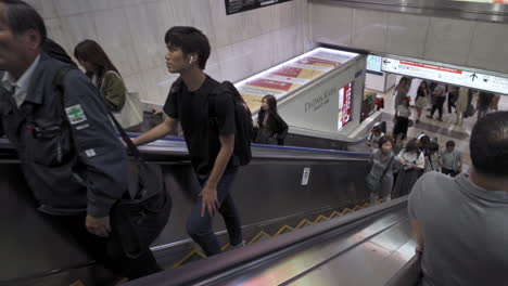 Pedestrians-using-the-escalator-with-a-few-people-in-a-rush-and-signage-overhead-in-Namba-Walk,-Osaka-Japan,-medium-shot