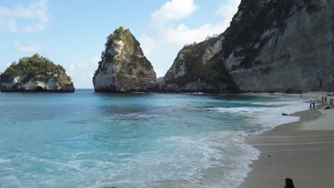 Schwenk-Von-Links-Nach-Rechts,-Um-Diamond-Beach-Freizugeben,-Während-Türkisfarbene-Wellen-An-Land-Spülen,-Eine-Bucht-Mit-Weißem-Sandstrand-Und-Nicht-Identifizierten-Personen-Im-Hintergrund