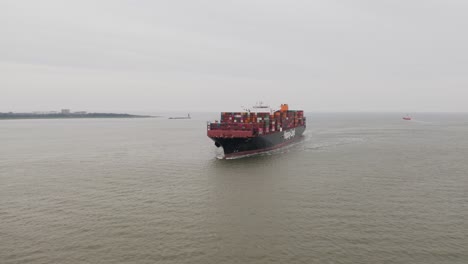 Aerial-of-Big-Containership-on-the-North-Sea-travelling-towards-the-port-of-Cuxhaven,-with-the-famous-Kugelbake-in-the-background