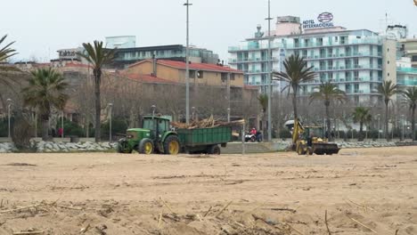 Yellow-backhoe-on-the-beach-helps-tractor-with-trailer-full-of-debris-to-move-forward-pushing-from-behind