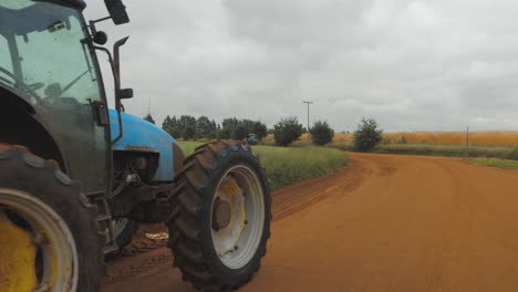 Slow-motion-shot-of-a-farm-tractor-pulling-a-trailer-with-empty-produce-crates-on-a-dirt-country-road-during-cloudy-day