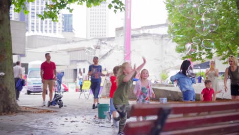 Bubble-man-street-entertainer-and-kids-playing-with-bubbles-in-London-riverside,-post-lockdown