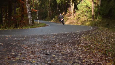 Motorbiker-on-a-curvy-road-through-a-autumn-forest-at-a-moody-day