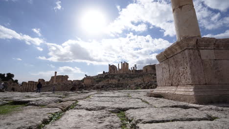 Toma-De-ángulo-Bajo-Del-Suelo-De-Piedra-De-La-Plaza-Ovalada-De-Ruinas-Romanas-En-La-Ciudad-De-Jerash-Con-Pilares-Corintios-Y-Estatuas-Al-Fondo