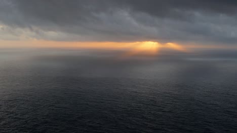 Sunset-over-ocean-with-dark-clouds-above,-high-point-view