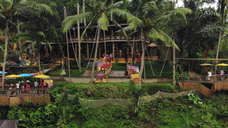 Stand-still-aerial-video-of-a-woman-enjoying-a-giant-swing-near-the-Tegenungan-Waterfall,-right-next-to-a-bar