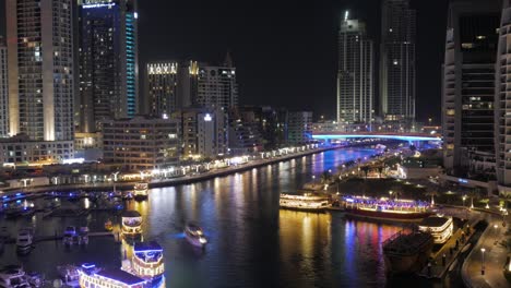 Ein-Wunderschöner-Zeitraffer-Des-Kanals-In-Der-Dubai-Marina:-Beleuchtete-Boote-Und-Yachten,-Die-Den-Wasserkanal-Befahren,-Nachtleben,-Wolkenkratzer-Im-Hintergrund