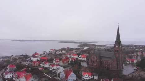 Flying-over-the-peaceful-red-city-of-Lysekil,-Sweden-with-a-beautiful,-old-style-cathedral-elevated-and-overlooking-the-land---Aerial-shot