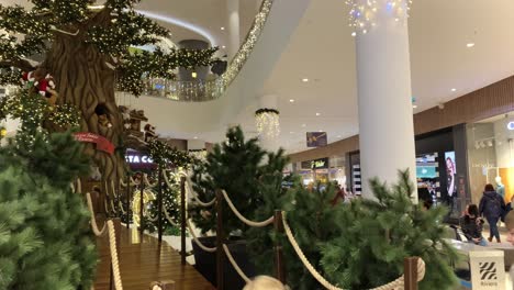 Close-up-christmas-tree-in-the-mall,-children-play-among-the-Christmas-decorations,-people-walk-and-shopping-around