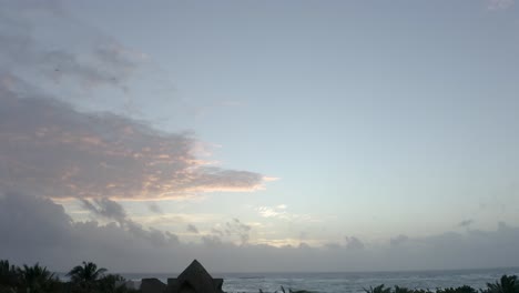 Early-Morning-Drone-Shot-of-the-Ocean-Lowering-to-Reveal-Beach-Huts-and-Palm-Trees