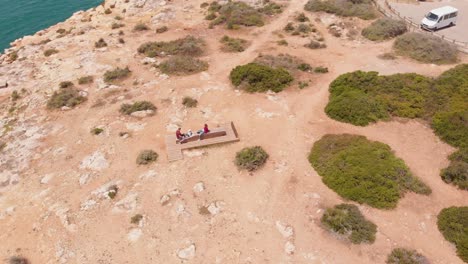 Aerial-orbiting-shot-over-seascape-promontory-Cliff-family-chill-on-beach,-Algarve