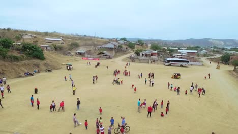 Eine-Gruppe-Afrikanischer-Kinder-In-Roten-Hemden-Spielt-Und-Rennt-Auf-Einem-Unbefestigten-Fußballfeld-Einer-Sportschulveranstaltung-Im-Dorf-Und-In-Der-Natur.-Ecuadorianische-Jungen-Rennen-Der-Drohne-Hinterher---Drohnenschuss-Fliegt-Davon