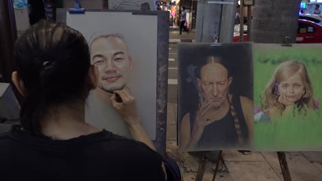 Back-view-of-street-artist-working-on-beautiful-realistic-portrait-paintings