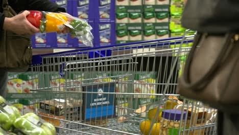 Hesitant-hands-of-woman-putting-bell-peppers-into-shopping-cart,-medium-shot