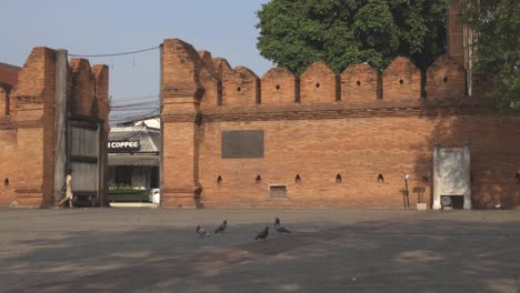 An-empty-courtyard-at-Thapae-Gate,-an-iconic-place-of-Chiang-Mai-city,-with-a-woman-wearing-face-mask-walking-by-on-a-weekday-morning-during-a-lockdown-due-to-COVID-19-pandemic