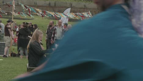 Merchandise-vendor-dances-by-her-stall-foreground-at-a-renaissance-fair,-Philadelphia-Renaissance-Fair,-Fort-Mifflin,-Pennsylvania