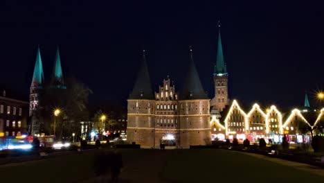 Zoom-out-time-lapse-of-Museum-Holstentor-western-gate-in-Lübeck,-Germany,-at-night-with-churches-in-the-background