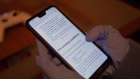 Closeup-Of-A-Young-Woman-Wearing-Latex-Gloves-While-Is-Scrolling-Down-News-About-Coronavirus