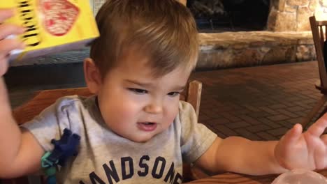 Young-boy-acting-silly-in-a-restaurant-watching-his-tablet,-device