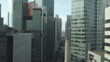 Up-rising-drone-shot-between-skyscraper-towers-in-singapore-city-center,-cars-traffic-in-the-middle