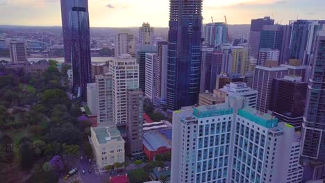 Panning-aerial-view-of-a-city-center-at-sunset-with-botanical-gardens-on-the-left