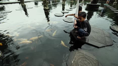 Kleine-Kinder-Füttern-Koi-Fische-Im-Wasserpalast-Tirta-Gangga-In-Bali,-Indonesien