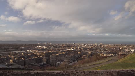 Panning-shot-from-Calton-hill-with-people-walking-in-the-foreground-with-nice-sunset-light-and-clouds-overlooking-the-city-of-Edinburgh,-Scotland-and-Atlantic-Ocean-in-the-background