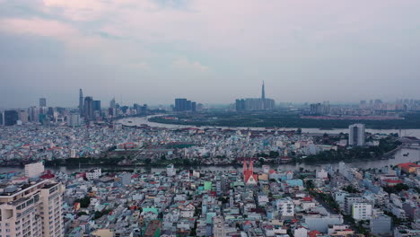 Abendlicher-Drohnenflug,-Der-Von-Der-Skyline-Von-Ho-Chi-Minh-Stadt-Zurückführt-Und-Wohngebiete,-Eine-Rote-Kirche-Und-Einige-Hochhäuser-Im-Vordergrund-Einschließt