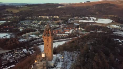 Aerial-orbital-shot-of-William-Wallace-Monument-in-Stirling,-Scotland,-during-blue-hour-on-a-cold-winter-evening