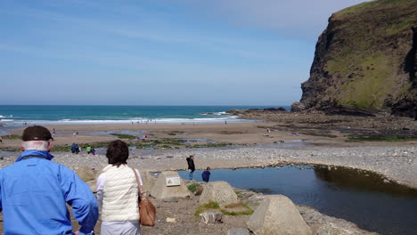 A-couple-of-senior-tourists-stop-at-Crackington-Haven-beach-in-Cornwall,-United-Kingdom,-where-walkers-swimmers-and-bathers-are-having-fun