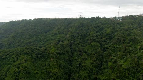 Nice-drone-forward-view-from-the-green-mountains-hillside-towards-the-big-ferris-wheel-from-Sky-Ranch-Theme-Park-on-the-top-from-Tagaytay-City,Philippines