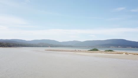 Drone-footage-over-sandy-beach-mountains-in-background