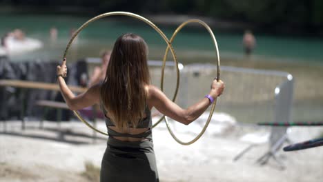 Mujer-Joven-Jugando-Con-Anillos-De-Hula-hoop-En-La-Playa,-Día-De-Verano,-Río-En-Segundo-Plano.