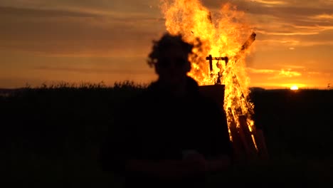 Silhouette-of-a-person-dancing-in-from-of-a-bonfire-in-the-sunset-with-a-drink-in-his-hand